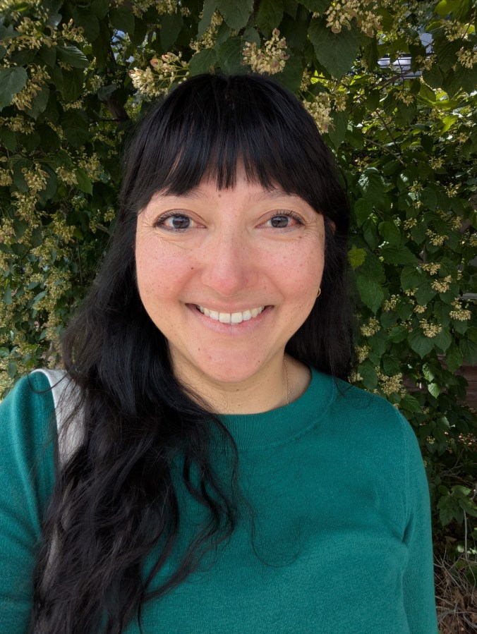 a picture of the author in a green sweater against a green-leaf background